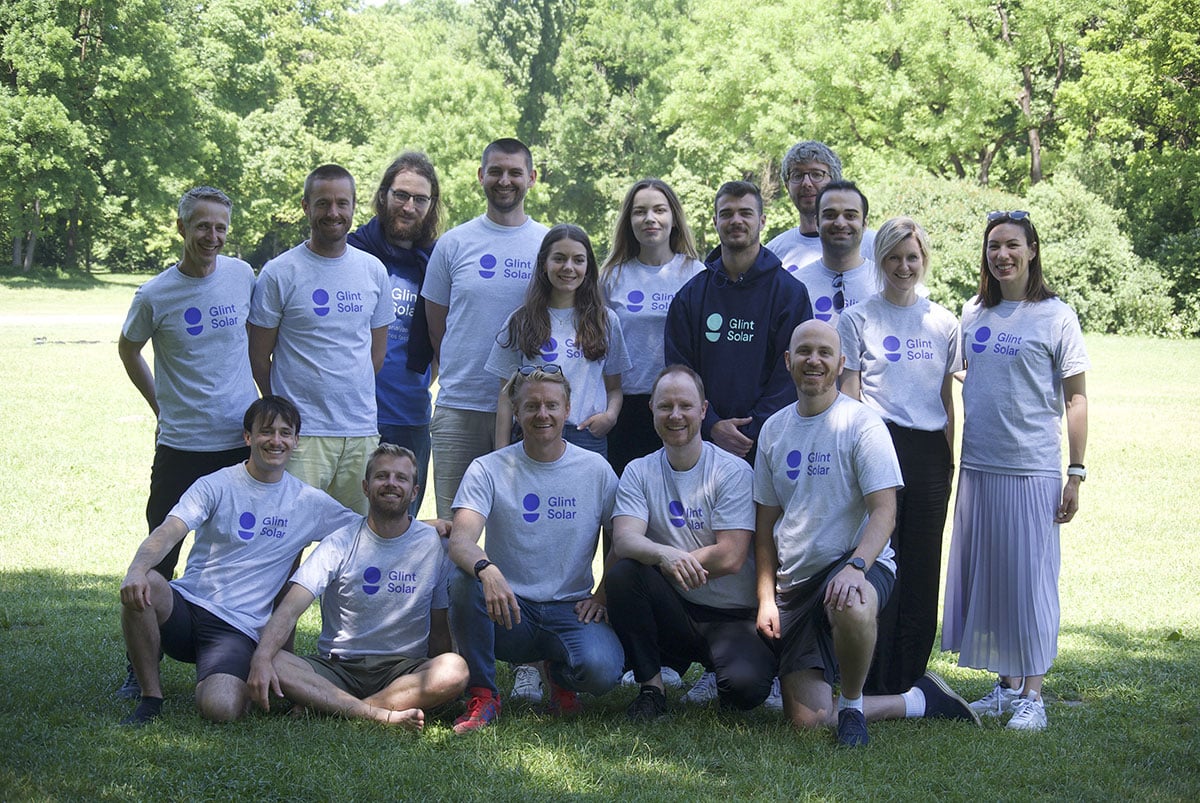 Glint Solar team members smile for a photo in Munich's English Garden, sunny with lots of trees around. They're all wearing Glint Solar T-shirts and one of them is wearing a Glint Solar hoodie.