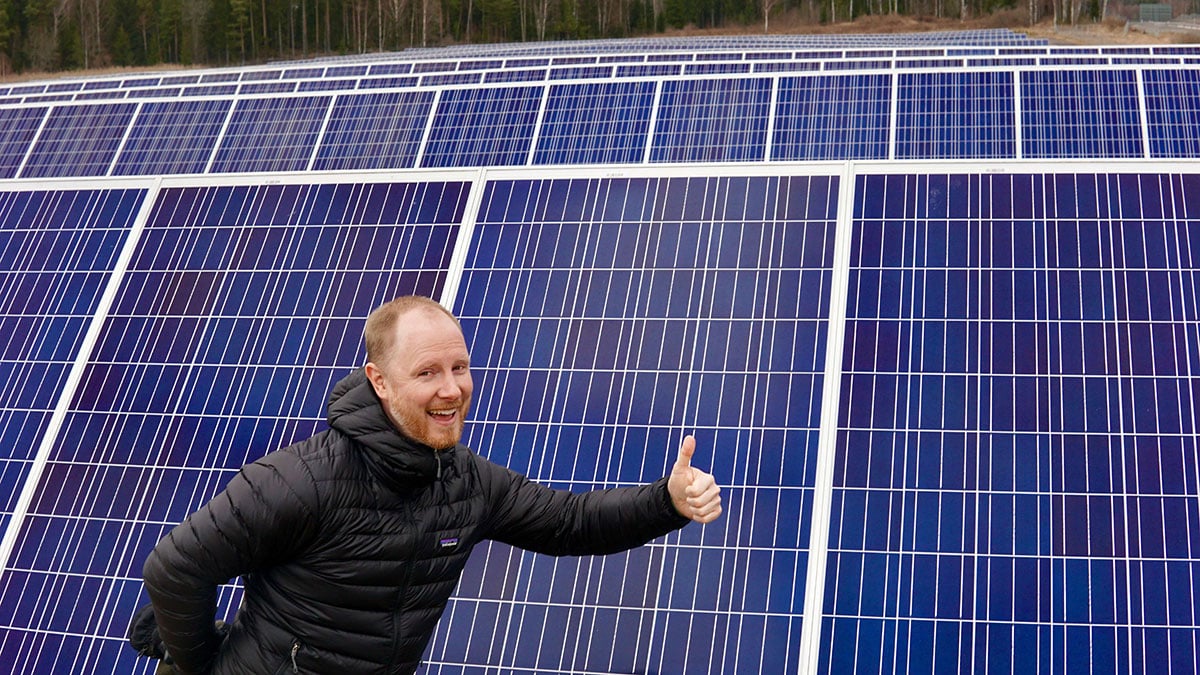 Lars, the Head of Design at Glint Solar, gives a thumbs-up in front of solar panels, wearing a black jacket and smiling.