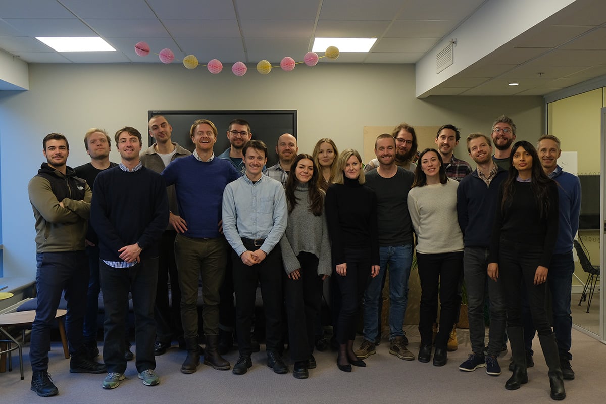 Nineteen Glint Solar team members, in casual greys, blues, blacks, and beiges, smiling together in the open office space.