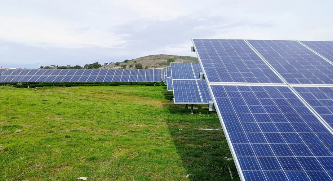 Rows of photovoltaic solar panels installed in a lush green field under a cloudy sky, signifying the growth of renewable energy.